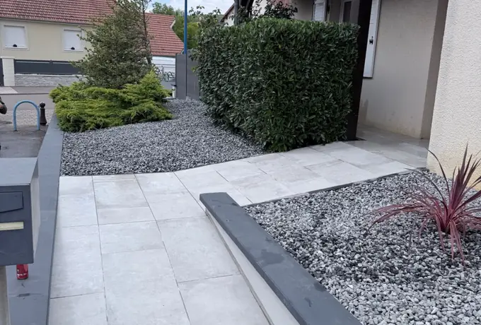 Allée dallée grand format avec bordures et gravier décoratif le long d'une haie