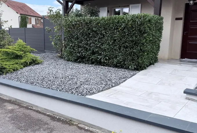 Entrée de maison avec dallage clair, gravier décoratif et haie de laurier taillée réalisée par Les Jardins d'Erwan