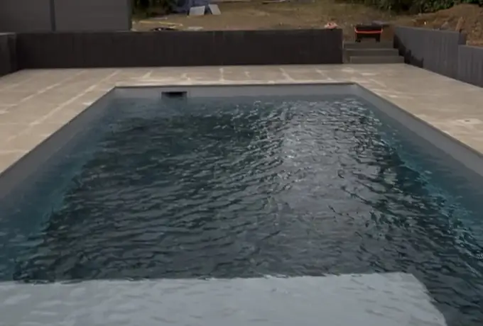 Piscine enterrée entourée d'une terrasse en dalles de pierre naturelle claire